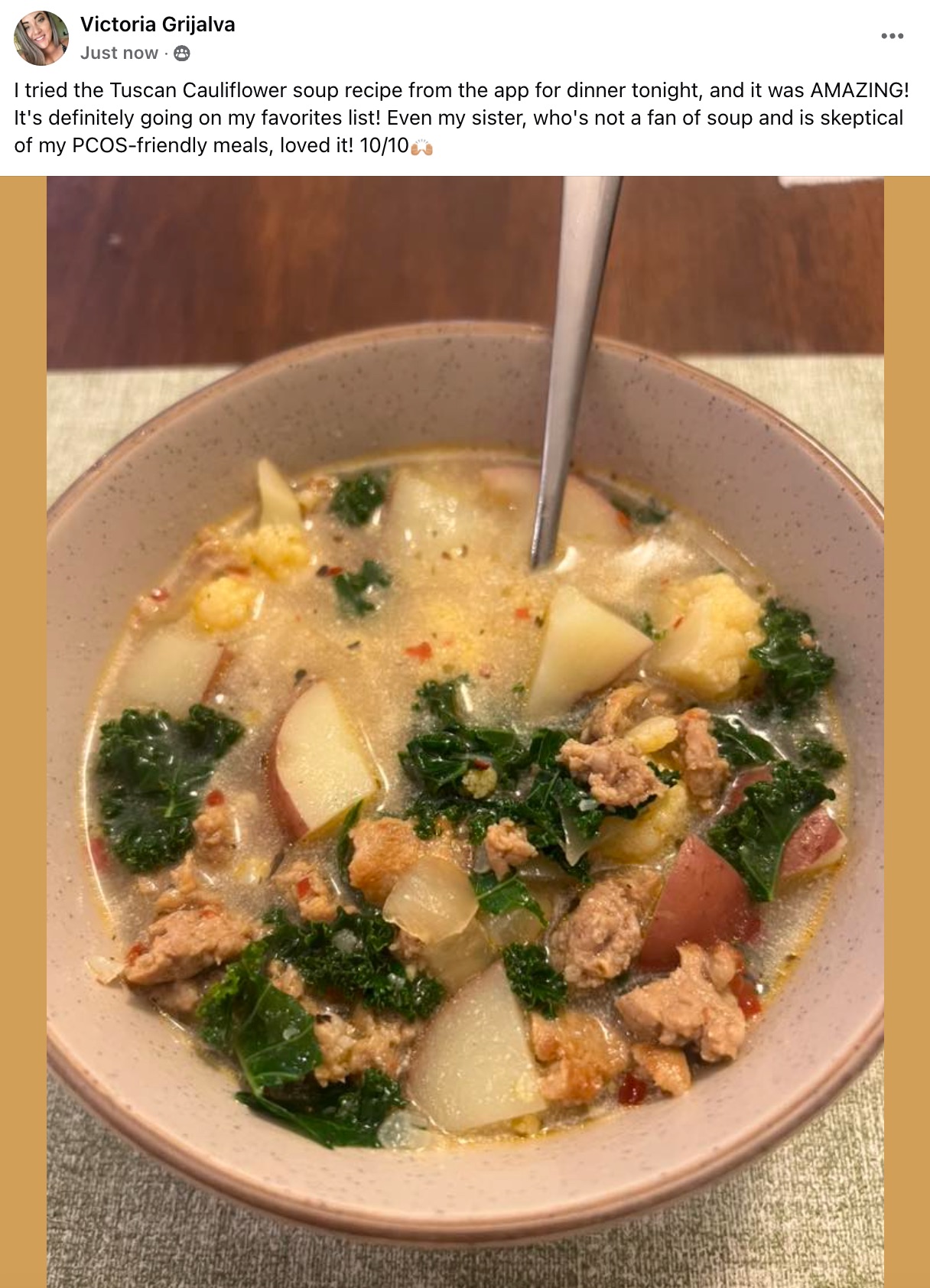 Bowl of creamy Tuscan-inspired soup with potatoes, kale, and crumbled sausage, spoon resting in the broth.