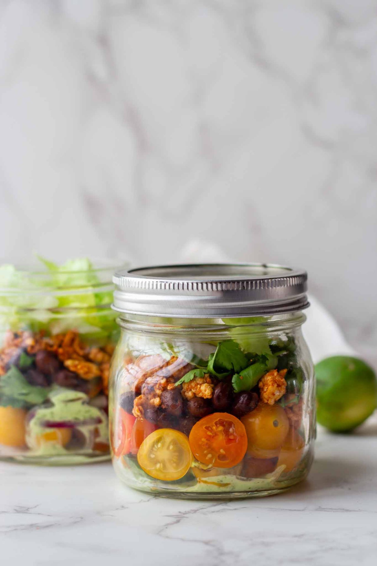 Mason jar salad with cherry tomatoes, greens, and crunchy toppings visible through a glass jar with a metal lid.
